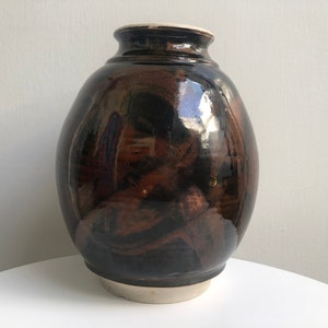 May include: A dark brown ceramic vase with a glossy finish. The vase has a rounded body and a slightly flared opening.