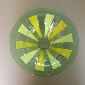 May include: A green glass bowl with a yellow and light green striped design. The bowl is round and has a wide rim.