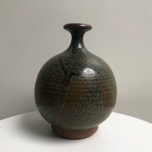 May include: A round, green and brown ceramic vase with a narrow neck.