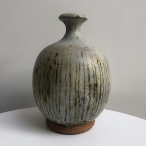 May include: A gray ceramic vase with a round body and a narrow neck. The vase has a textured surface with vertical lines and brown and blue accents.