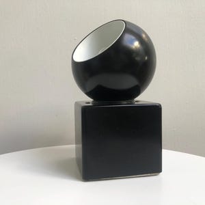 May include: A black and white table lamp with a round, angled shade and a square base.