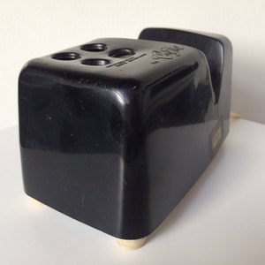 May include: Black plastic pencil sharpener with a gold-colored base and four holes for pencils. The sharpener has a label that reads "C.R. Gibson, Made in U.S.A."