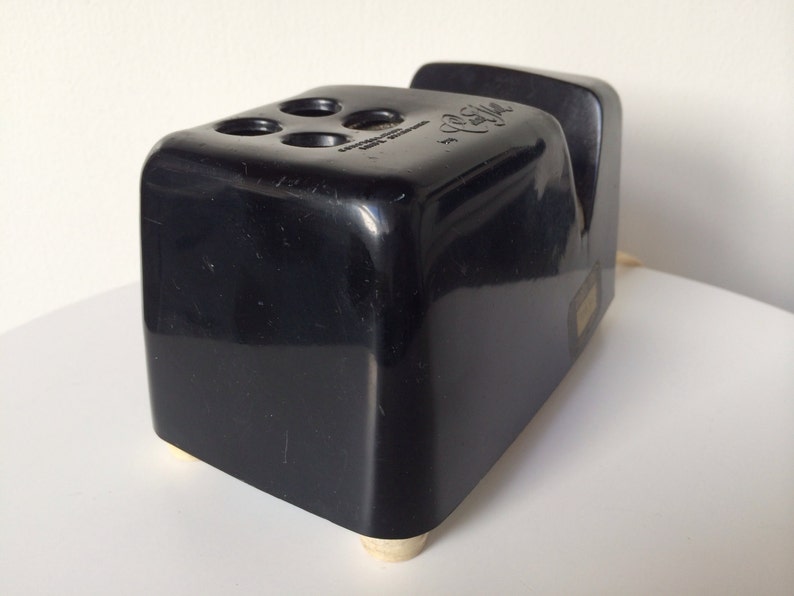 May include: Black plastic pencil sharpener with a gold-colored base and four holes for pencils. The sharpener has a label that reads "C.R. Gibson, Made in U.S.A."