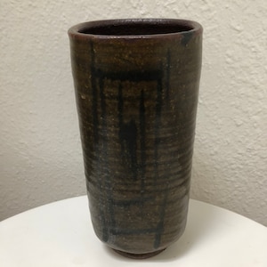 May include: A brown ceramic vase with black brushstrokes. The vase has a rounded bottom and a cylindrical shape.