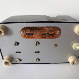 May include: A silver and black electric knife sharpener with a copper-colored label that reads "Carvel Hall Electric Knife Sharpener Chas. D. Briddell Inc. Crisfield, MD".