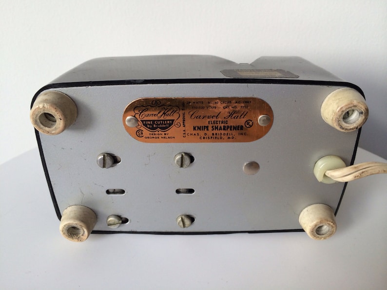 May include: A silver and black electric knife sharpener with a copper-colored label that reads "Carvel Hall Electric Knife Sharpener Chas. D. Briddell Inc. Crisfield, MD".