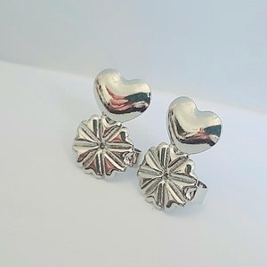 Può includere: Un paio di orecchini d'argento con la parte superiore a forma di cuore e la parte inferiore a forma di fiore.