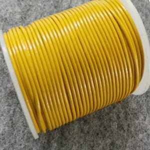 Puede incluir: Un carrete de cordón de cuero amarillo brillante. El cordón está enrollado firmemente alrededor de una bobina de plástico blanco. El cordón tiene un acabado liso y brillante. El fondo es gris neutro.