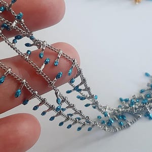 May include: A silver chain with blue teardrop-shaped beads hanging from it. The chain is layered and has a delicate, intricate design.