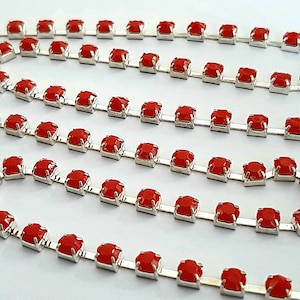 May include: A silver chain with red square rhinestones. The chain is made of metal and has a shiny finish. The rhinestones are evenly spaced and create a sparkling effect.