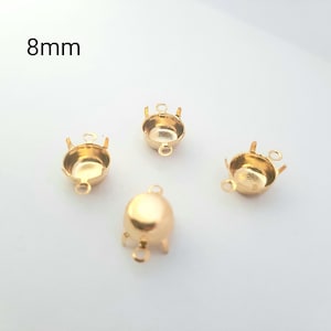 May include: Four gold-colored jewelry findings, each with a unique design. The text "8mm" is visible in the upper left corner. These findings are likely used for jewelry making, with a small loop for attaching to other components.