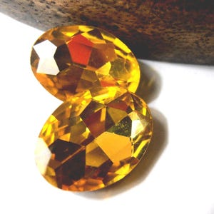 Può includere: Due gemme di vetro di forma ovale, sfaccettate, di colore ambrato.