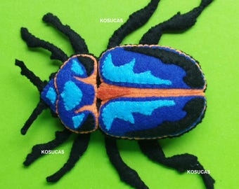 May include: A felt bug with a blue and orange design on a green background. The bug has black legs and antennae. The text "PDF PATTERN" is at the top of the image.