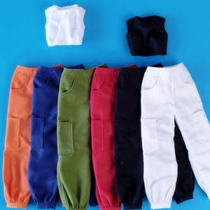 May include: A collection of doll clothes, including cargo pants in orange, blue, green, red, black, and white, and two sleeveless tops, one white and one black. The items are arranged on a blue background.