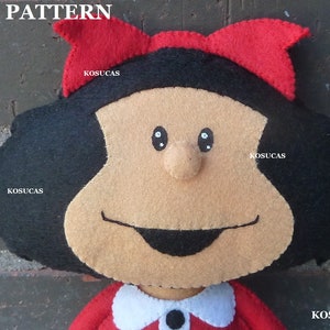 May include: A felt doll with black hair, a red bow, and a smiling face. The doll is wearing a red dress with a white collar and a black button.