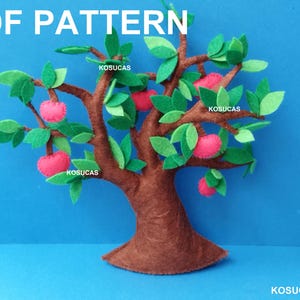 Może przedstawiać: Filcowe drzewo z brązowym pniem i gałęziami, zielonymi liśćmi i różowymi jabłkami. U góry napis "PDF PATTERN". Tło jest jednolicie niebieskie.