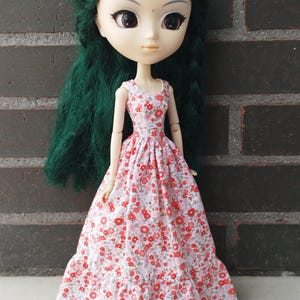 May include: A doll with long green hair wearing a white dress with a red floral pattern.