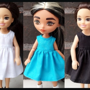 May include: Three dolls dressed in sleeveless dresses in white, turquoise, and black. The dresses have a simple, classic design. The dolls have different skin tones and hairstyles. The word "KOSUCAS" is in the lower left corner.