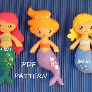 May include: Three felt mermaid dolls with different coloured hair and tails. The mermaids are wearing seashell-shaped sequins. The text "PDF PATTERN" is printed below the mermaids.