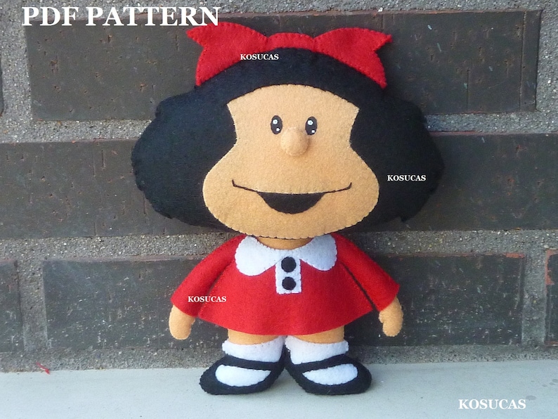May include: A felt doll of a girl with black hair, a red dress, and a red bow. The doll has a white collar with two black buttons. The doll is standing in front of a brick wall.
