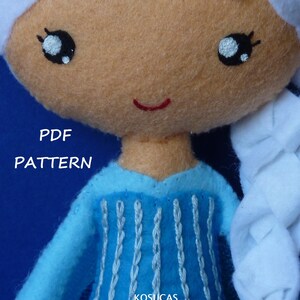May include: A blue felt doll with white hair, a blue dress with white embroidery, and a red smile. The doll is holding a white felt braid. The text "PDF PATTERN" and "KOSUCAS" is visible on the image.
