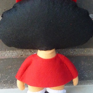 May include: A felt doll pattern for a girl with black hair and a red dress. The pattern includes instructions for making the doll's hair, dress, and shoes.