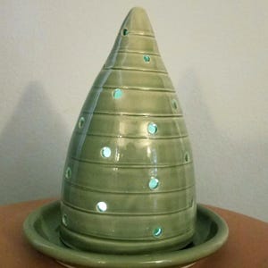 May include: A green ceramic cone-shaped lamp with a base. The lamp has a series of holes around the sides and a light shines through the holes.