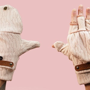 Op de afbeelding: Lichtbeige converteerbare gebreide handschoenen met een kabelgebreid patroon. De handschoenen hebben een klep die kan worden vastgezet om de vingers bloot te leggen. Een bruin leren label met de tekst "ProperFit" is bevestigd.