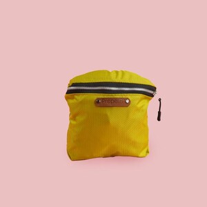 Puede incluir: Una peque&ntilde;a bolsa amarilla con cremallera, con una cremallera negra y una etiqueta de cuero marr&oacute;n que dice "PROSPER"