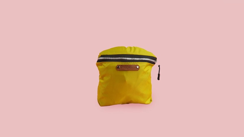 Puede incluir: Una peque&ntilde;a bolsa amarilla con cremallera, con una cremallera negra y una etiqueta de cuero marr&oacute;n que dice "PROSPER"