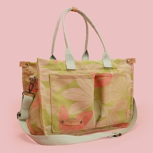 May include: A floral print tote bag with a shoulder strap and two handles. The bag features a light green and pink floral pattern on a beige background. It has two front pockets and a light green strap and handles.