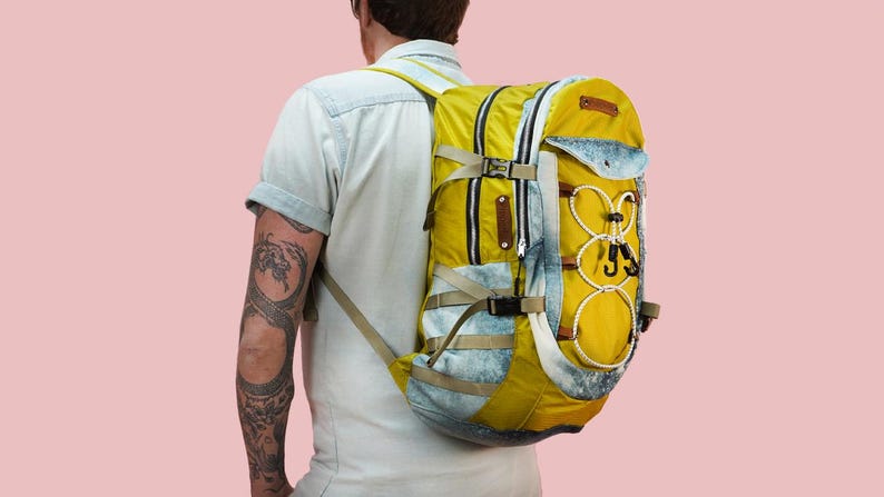 Puede incluir: Una mochila amarilla y azul con m&uacute;ltiples correas y hebillas. La mochila tiene un patr&oacute;n de tie-dye blanco y azul en la parte delantera.