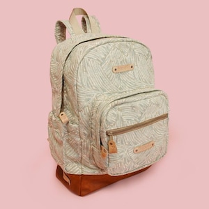 May include: A backpack featuring a light grey fabric with a white palm leaf pattern, a brown leather-like base, and brown leather-like accents on the front pocket and top handle. The bag includes a front zippered compartment and side pockets.