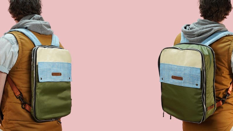 Pode incluir: Duas mochilas com um design de blocos de cores s&atilde;o mostradas por tr&aacute;s. As mochilas t&ecirc;m uma parte superior creme, um centro azul claro e uma parte inferior verde oliva. As al&ccedil;as s&atilde;o azuis claras e as mochilas t&ecirc;m uma etiqueta de couro castanho.