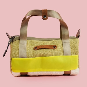 May include: A small, green and yellow canvas tote bag with a brown leather strap and a zipper closure. The bag has a white fluffy lining and a brown leather patch with the word "Everyday" printed on it.