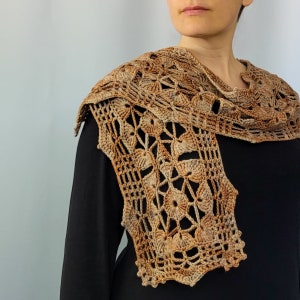May include: A brown crocheted shawl with a delicate floral pattern. The shawl is draped over a person's shoulders and is made with a light brown yarn.