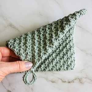 A hand folds the sage green Folded Potholder to show its double-thick construction and distinctive folded design.