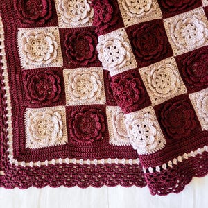May include: A handmade crochet blanket in a checkerboard pattern. The squares alternate between a deep burgundy and a light beige, each featuring a raised floral design. The blanket has a scalloped edge in burgundy.