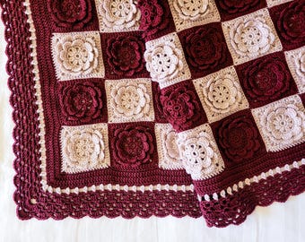 May include: A handmade crochet blanket in a checkerboard pattern. The squares alternate between a deep burgundy and a light beige, each featuring a raised floral design. The blanket has a scalloped edge in burgundy.