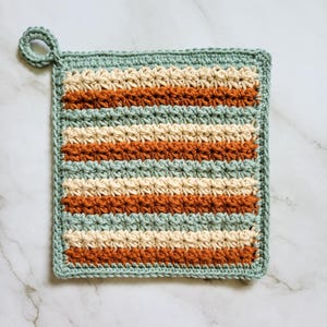 Three-color Classic Potholder crocheted in alternating rows of rust, beige, and sage green Trinity Stitch. The dense, double-thick fabric features a hanging loop and is displayed on a white marble countertop.