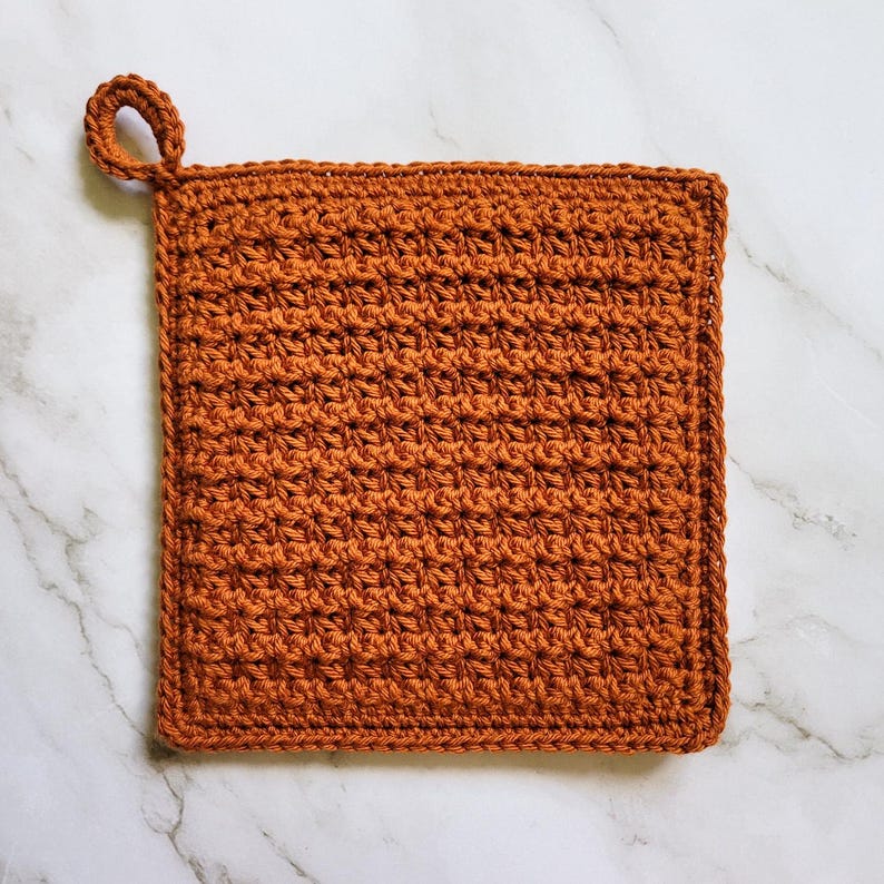 Rust-colored Classic Potholder crocheted in dense, double-thick Trinity Stitch fabric with a hanging loop. The potholder is displayed on a white marble countertop.