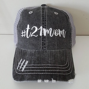 May include: A black and gray distressed trucker hat with a white embroidered design that says "#t21mom".