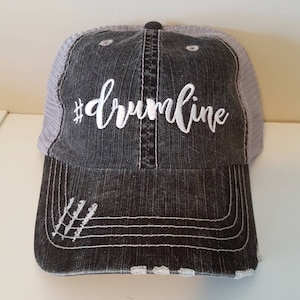 May include: A black and grey distressed trucker hat with a white embroidered hashtag and the word "drumline".