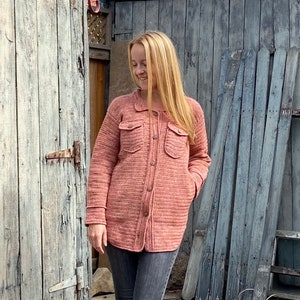 May include: A pink crocheted button-up jacket with pockets. The jacket is made with a textured yarn and has a relaxed fit.