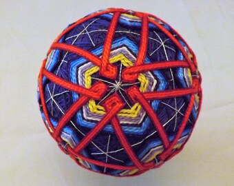 Japanese Temari Ball handmade rice hulls with a bell inside 12 yellow and blue shapes with 20 red spinners over Purple
