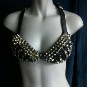 May include: A black leather bra with silver metal studs and beads. The bra has adjustable straps.