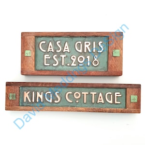 May include: Two wooden signs with green ceramic tiles. The top sign reads "Casa Gris Est. 2018" and the bottom sign reads "Kings Cottage".