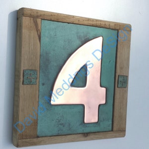Op de afbeelding: Een houten huisnummerbord met een koperen nummer vier op een teal groene achtergrond.
