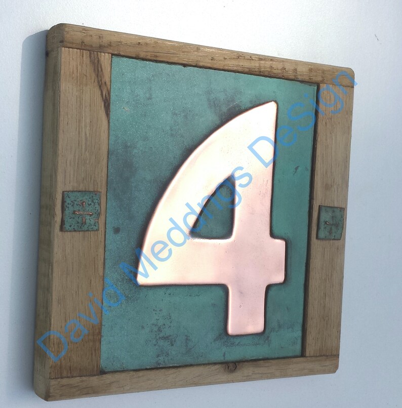 Op de afbeelding: Een houten huisnummerbord met een koperen nummer vier op een teal groene achtergrond.