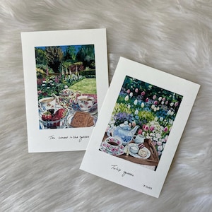 Puede incluir: Dos pinturas de acuarela sobre papel blanco. Una representa un servicio de té en un jardín con el texto "Tea served in the garden". La otra muestra un servicio de té en un jardín de tulipanes con el texto "Tulip garden" y la fecha "7.2023."